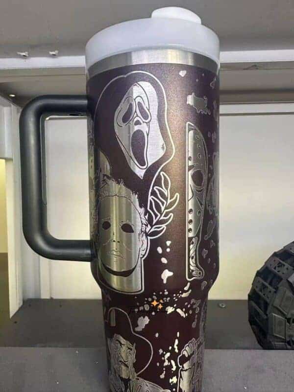 Dark-themed coffee tumbler with spooky ghost and horror mask illustrations.