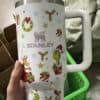 Decorative Christmas-themed mug with Santa, elf, reindeer, holly, and gift graphics.